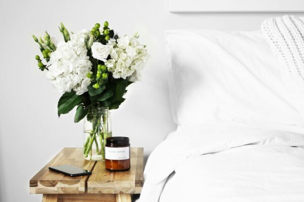 white bedroom interiors showing a white bedside table with a vase of flowers