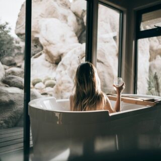 Woman unwinding in her bath looking out onto the natural rocky environment outside the full glass windows